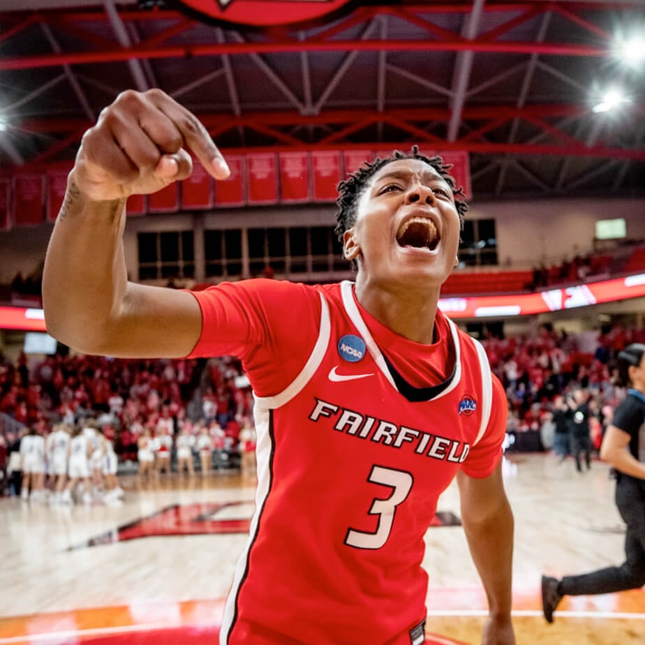 A ɫƬ University woman basketball player in a red jersey joyfully celebrates on the court, showcasing their excitement and team spirit.